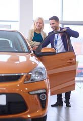 Dealer with woman stands near a new car in the showroom