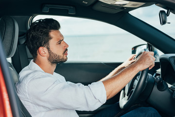 handsome man in white shirt driving car and looking away