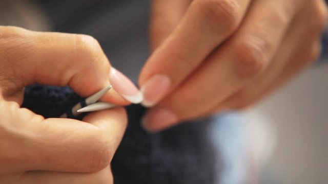 Close-up footage of woman knitting clothing item with blue threads