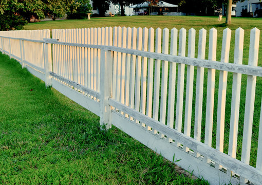 An authentic white picket fence in warm evening light stretches into the distance.