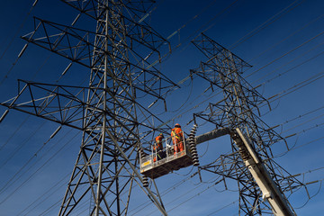 Hydro linemen on boom lift removing old suspension insulators on high voltage power line tower