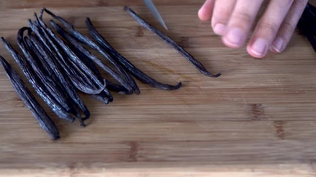 Slicing vanilla beans with a knife on wooden cutting board, close up