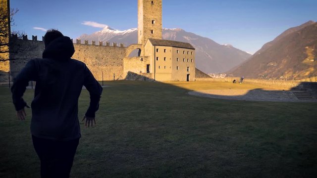A young adult male performs a cartwheel on the grassy courtyard of the Grazzano Visconti castle. Slowmo. Full shot.