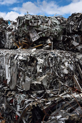Dump with bales of crushed recycled scrap metal and blue sky clouds