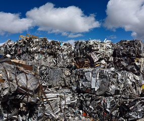 Mountain of crushed recycled scrap metal cubes with blue sky clouds
