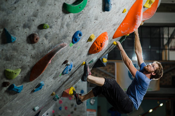 strong healthy sport caucasian man with beard and eyeglasses climbing on wall indoors during bouldering exercise - obrazy, fototapety, plakaty