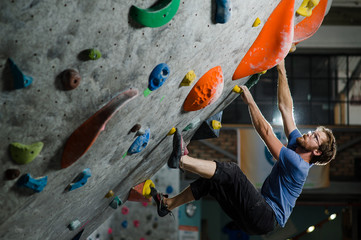 strong healthy sport caucasian man with beard and eyeglasses climbing on wall indoors during bouldering exercise