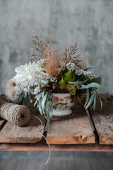 bouquet of white flowers in a glass jar in the hands of a girl florist on the background of a concrete wall.