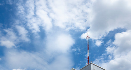red and white telecommunication pole on roof of building with blue sky and white cloud background on bright day.