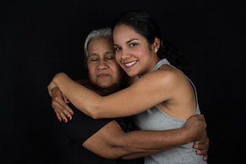 Cheerful woman embraces older woman with close eyes. Black background