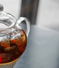 Hot scented tea with goji chinese wolfberries in transparent glass teapot on porcelain base with copy space