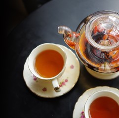 Black tea with goji (chinese wolfberries) and jasmine in transparent glass teapot and 2 porcelain cups with flower pattern saucers on black table top view