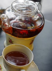 Black tea with chinese wolfberries and jasmine in transparent glass teapot and 2 porcelain cup with flower pattern saucer on black table