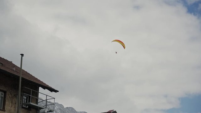Figure of skydiver with colorful yellow red parachute against cloudy sky