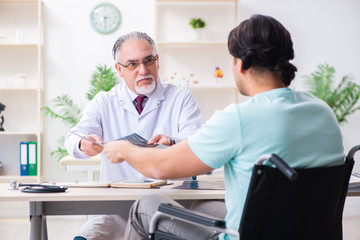Fototapeta premium Male patient in wheel-chair visiting old doctor
