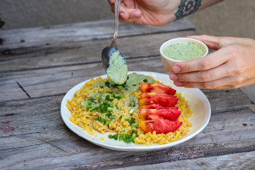 Bulgur with sauce, greens, tomatoes on plate. Vegan lunch.