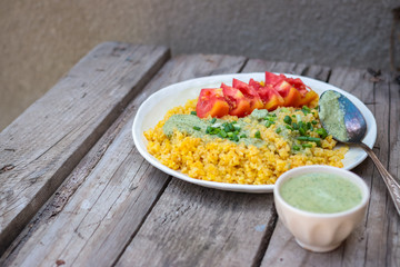 Bulgur with sauce, greens, tomatoes on plate. Vegan lunch.