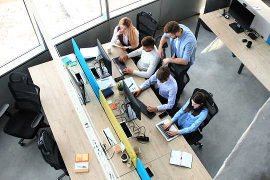 Top view of young modern colleagues in smart casual wear working together while spending time in the office.