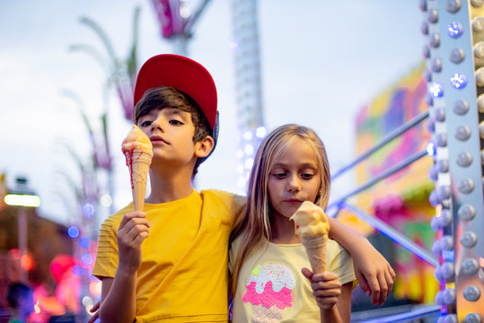 Smiling girl and boy eating ice cream in Funfair Park lights carnival