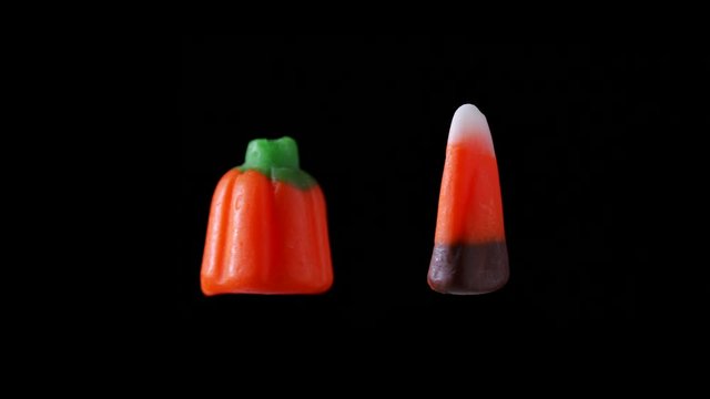 Candy corn and a candy pumpkin are seen floating and rotating with a black background.