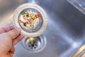 Hand holding kitchen sink waste filter with trapped food waste