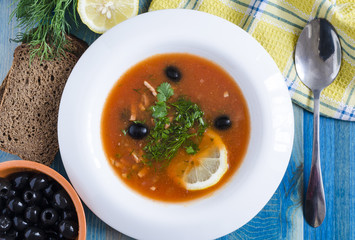soup with meat and vegetables in white plate on blue background black bread and lemon on background