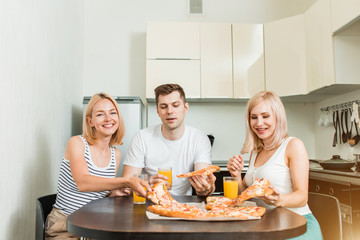 Young friends eating pizza in kitchen and smiling