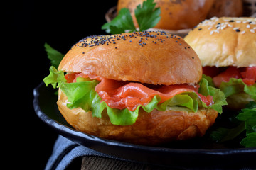 Bagel sandwich with smoked salmon and lettuce salad on black plate