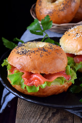 Bagel sandwich with smoked salmon and lettuce salad on black plate