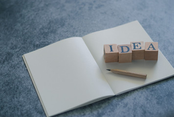 Photo of bright letter IDEA wood cube block on notebook with pencil on black background with copy space. Positive concept of business, creativity, education, knowledge, learning and studying.