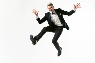 Portrait of young smiling handsome showman in tuxedo stylish black suit, studio shot jumping at...