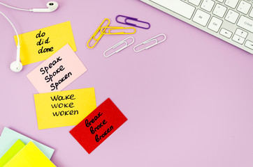 Top view desk with earphones, keyboard and sticky notes with handwritten irregular verbs. Flat lay...