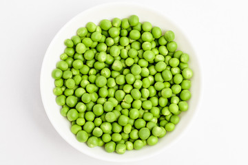 Freeh organic green peas in a white round bowl on a table in soft focus, isolated on white, top view