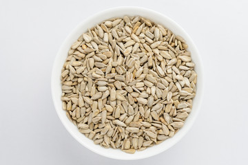 Freeh raw organic sunflower seeds in a white round bowl on a table in soft focus, isolated on white, top view