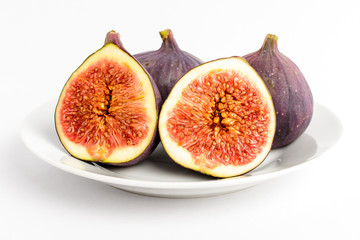 Fresh ripe organic figs on a white table, two whole figs and one sectioned in two parts, close up with soft focus, side view