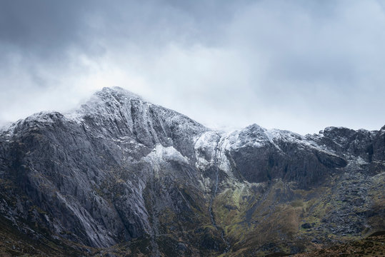 Stunning dramatic landscape image of snowcapped Glyders mountain range in Snowdonia during Winter with menacing low clouds hanging at the peaks