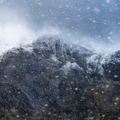 Stunning dramatic landscape image of snowcapped Glyders mountain range in Snowdonia during Winter with menacing low clouds hanging at the peaks