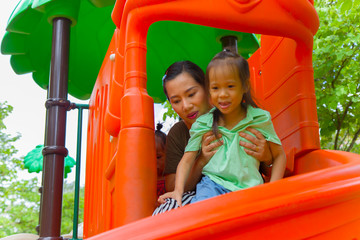 Mom and daughter  playing on play ground play slider seesaw,  Funny Asian family in a park