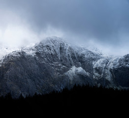 Stunning dramatic landscape image of snowcapped Glyders mountain range in Snowdonia during Winter with menacing low clouds hanging at the peaks