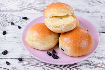 Yeast buns with raisins and butter on ceramic plate on white wooden table