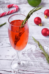 Red alcoholic drink in a tall glass surrounded by Christmas attributes against white wooden background