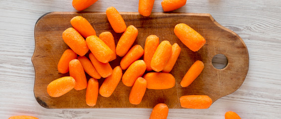 Fresh baby carrots on a rustic wooden board on a white wooden surface, top view. Overhead, from above, flat lay. Close-up.