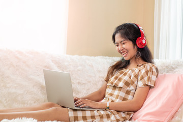 Young Asian woman enjoy listening to music with headphones and using laptop, happy and relaxing time