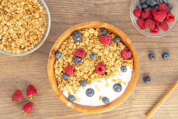 Breakfast smoothie bowl with granola, fresh raspberries, blueberries and yogurt on wooden background.