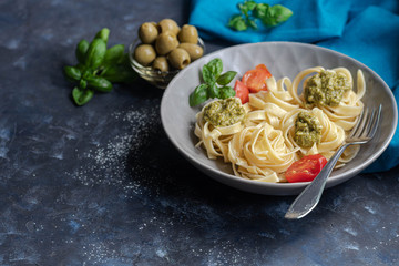 Tagliatelle cooked aldente with pasta pesto. Near bowl with sauces, physalis, olives. The noodles are decorated with green sprigs of basil. Healthy life experience. Proper nutrition. Vegetarian dish. 