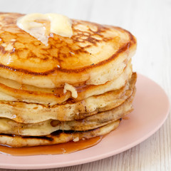 Homemade pancakes with butter and maple syrup on a pink plate, side view. Close-up.