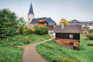 Fototapeta premium Misty autumn cityscape of Altaussee town with Heiliger Agidius church on background, district of Liezen in Styria, Austria. Beauty of countryside concept background.