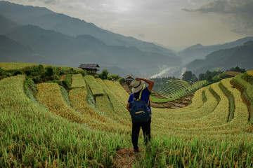Fototapeta premium Hipster girl standing holding a hat. The atmosphere rice terraces in the evening. There are mountains behind the scenes. at Mu Cang Chai in Vietnam.