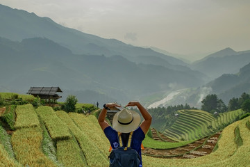 Hipster girl standing mark hand is heart. The atmosphere rice terraces in the evening. There are mountains behind the scenes at Mu Cang Chai in Vietnam.