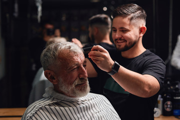 smiling awesome young barber brushing the hair of senior man, preparing to cut hair